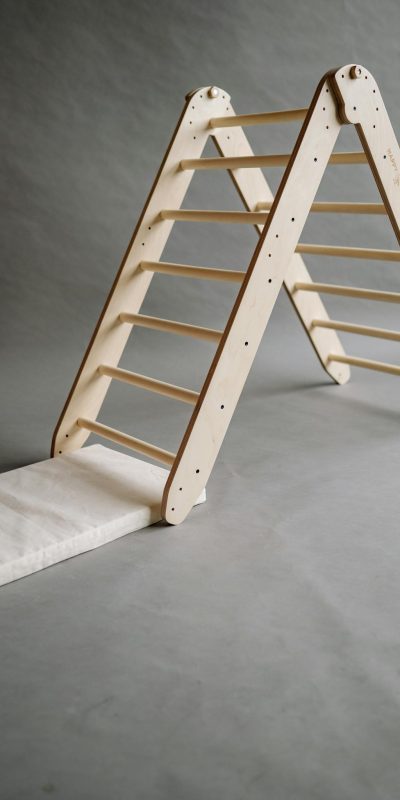 A minimalist wooden toy ladder against a gray playroom background.