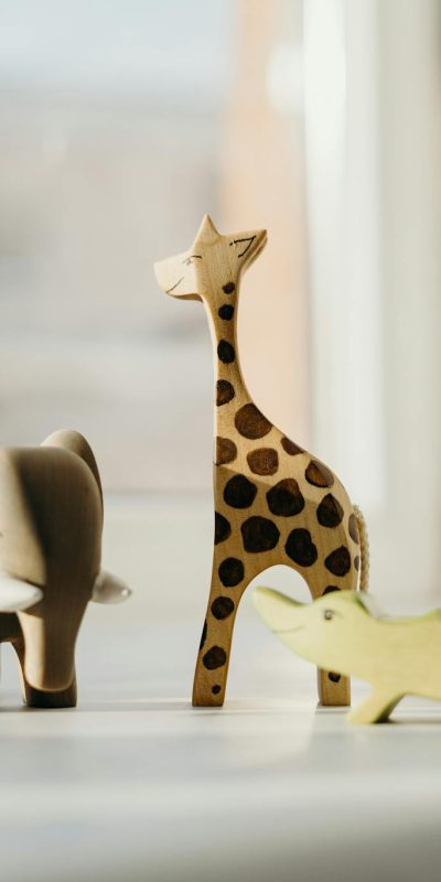 Set of wooden animal toys including giraffe, elephant, and crocodile on a sunny windowsill.