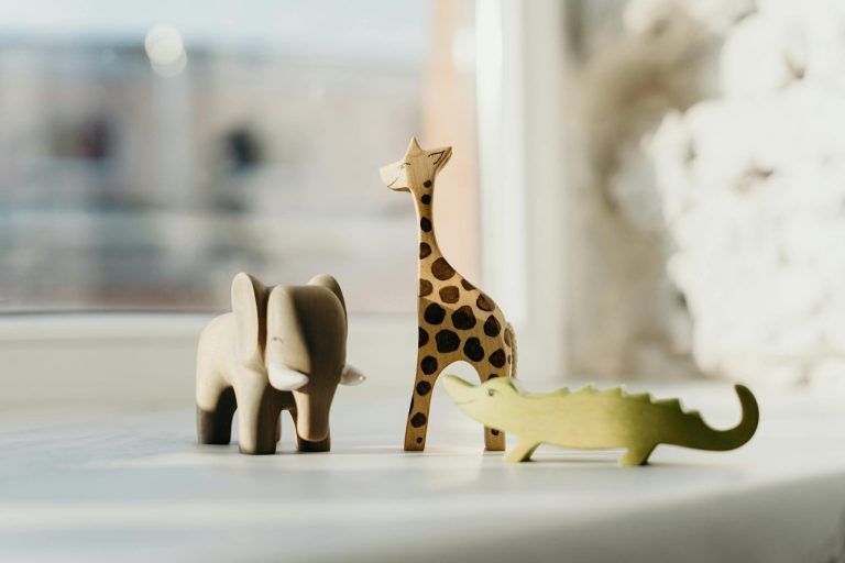 Set of wooden animal toys including giraffe, elephant, and crocodile on a sunny windowsill.