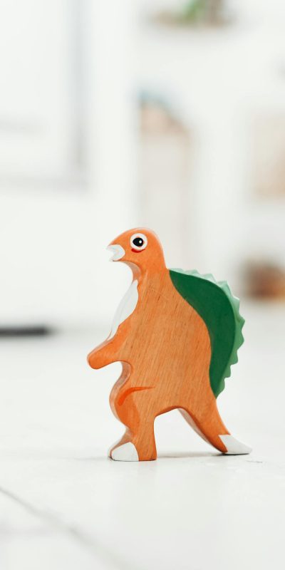 Vibrant wooden dinosaur toy standing on light indoor floor in playroom.